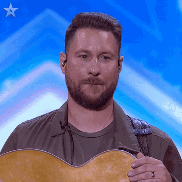 a man with a beard is holding a guitar in front of a blue background with a star