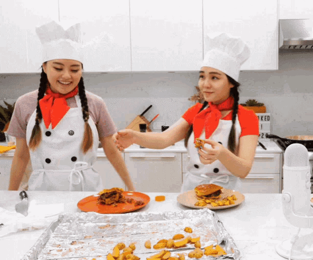 two women wearing chef 's hats and aprons are standing in a kitchen