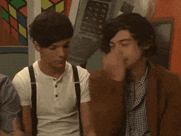 two young men sitting next to each other with one wearing suspenders and the other wearing a brown cardigan