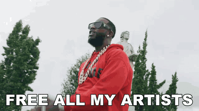 a man in a red hoodie stands in front of a statue with the words free all my artists