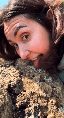 a woman laying on a rock with her head in the dirt making a funny face