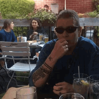 a man with a tattoo on his arm is sitting at a table drinking a drink