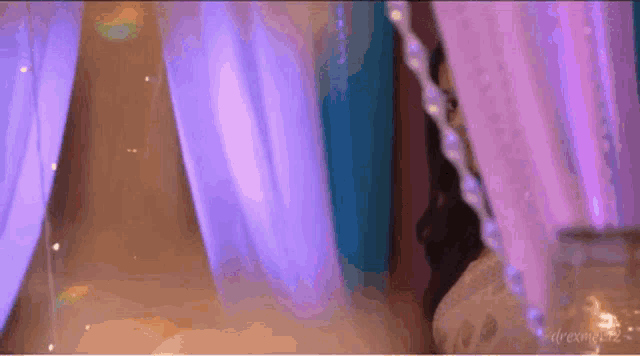 a woman is standing in a room with purple curtains and candles .