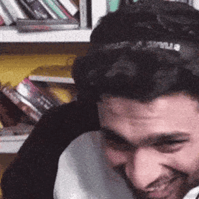 a man wearing a headband that says ' jesus ' on it smiles in front of a bookshelf
