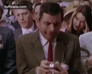 a man in a suit and tie is sitting in a crowd of people holding a camera .