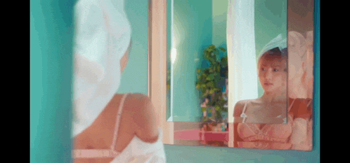 a woman with a towel wrapped around her head looks at her reflection in a mirror .
