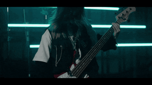 a woman is playing a bass guitar in a dark room with a lot of lights behind her .
