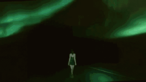 a woman in a green dress is walking down a dark street in the dark .