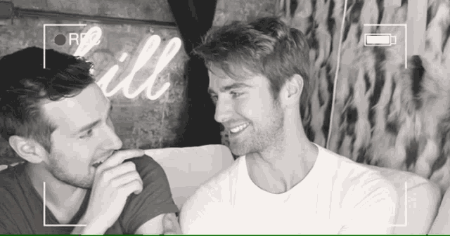 two men are laughing in front of a sign that says will