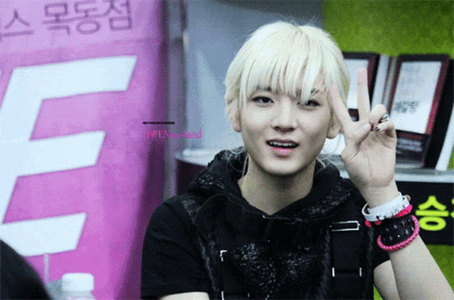 a young man giving a peace sign in front of a pink e