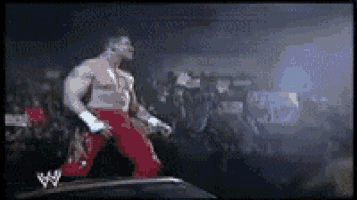 a wrestler in red pants and white gloves is walking on a ramp in front of a crowd .