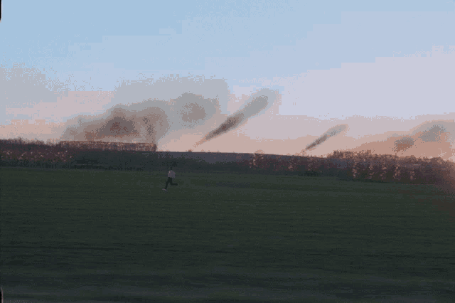 a man is running in a field with smoke coming out of the trees