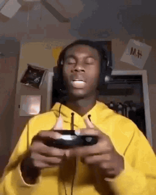 a man wearing headphones and a yellow hoodie is playing a video game with a controller .