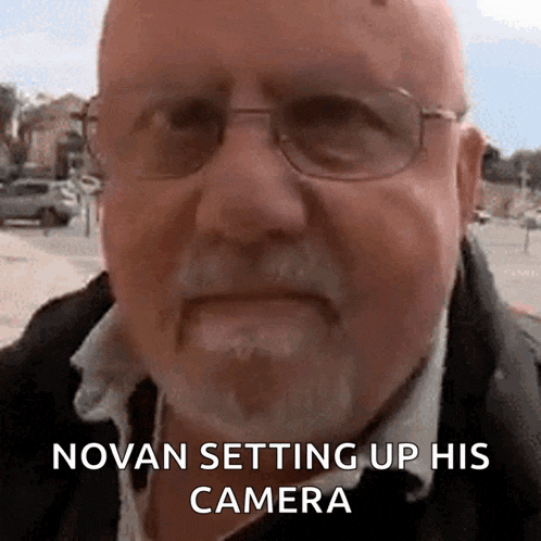 a man with glasses and a beard is talking about novan setting up his camera
