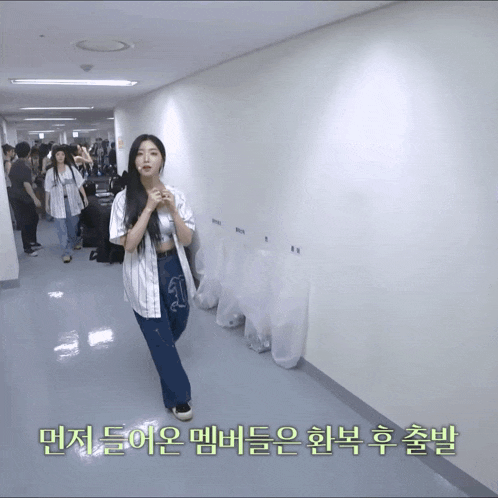 a woman walking down a hallway with korean writing on the wall behind her