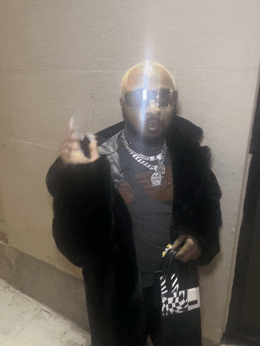 a man wearing sunglasses and a fur coat is holding a bag and giving the middle finger