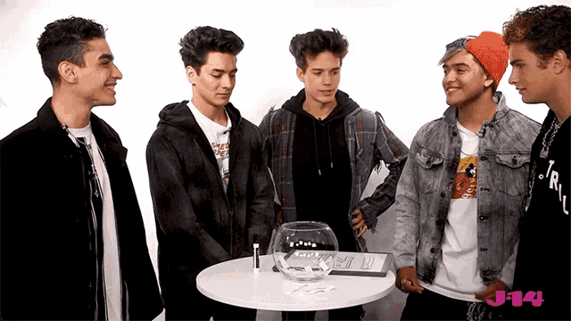 a group of young men standing around a table with j-14 written in pink