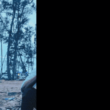 a man in a white shirt is talking on a cell phone in front of trees with the letter r above him