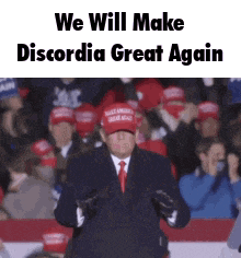 a man in a suit and tie is standing in front of a crowd wearing a maga hat and gloves .