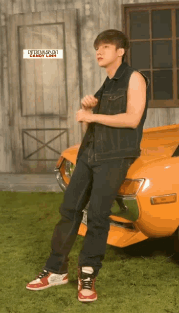 a young man standing next to an orange car with a sign above him that says entertainment