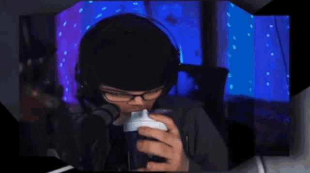 a man wearing headphones and glasses is drinking from a cup