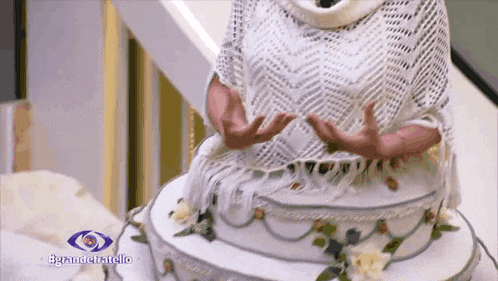 a woman in a white sweater is standing next to a wedding cake with the words grandefratello on the bottom