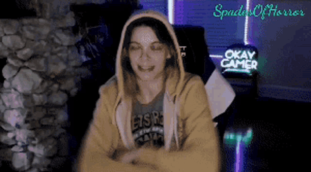 a woman in a yellow hoodie is sitting in front of a okay gamer sign