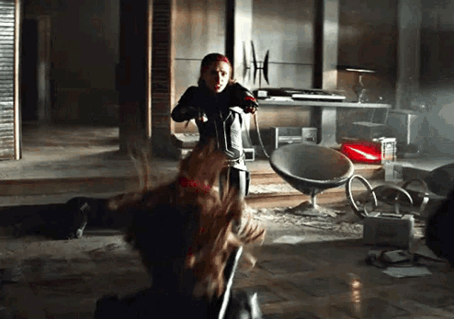 a woman in a black suit is holding a gun in a dark room .