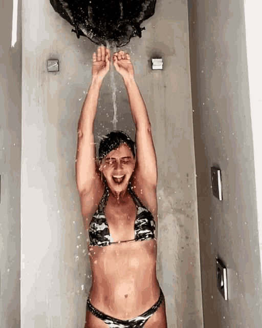 a woman in a bikini is taking a shower with her arms up