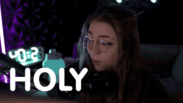 a woman wearing glasses is sitting in front of a microphone and the word holy is on the screen