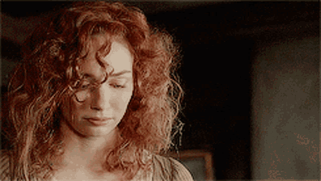 a woman with red curly hair looks down at something