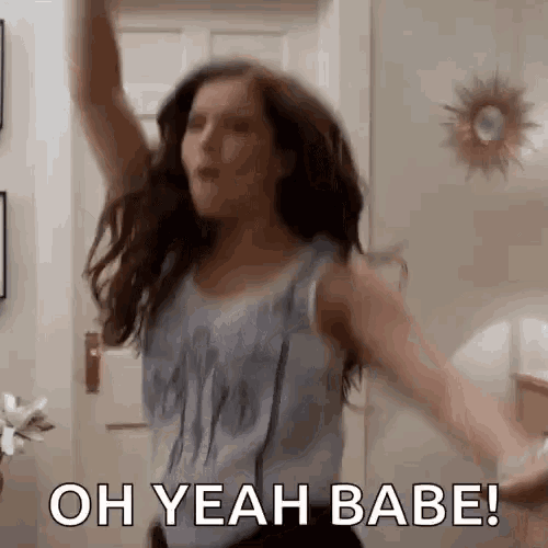 a woman is dancing in a living room with her arms in the air and the words `` oh yeah babe '' .