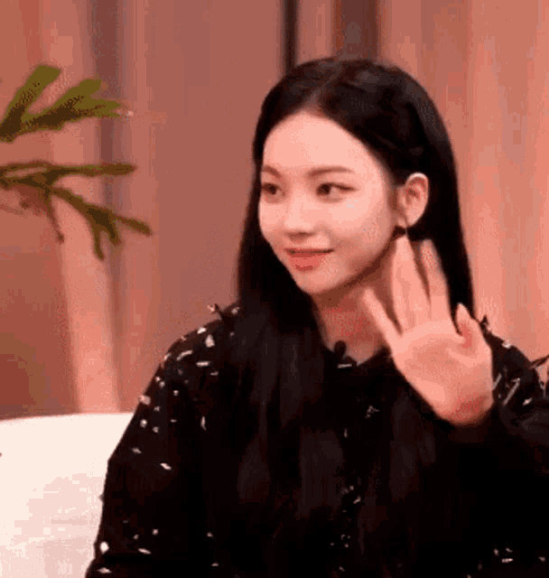 a woman is sitting on a couch waving at the camera .