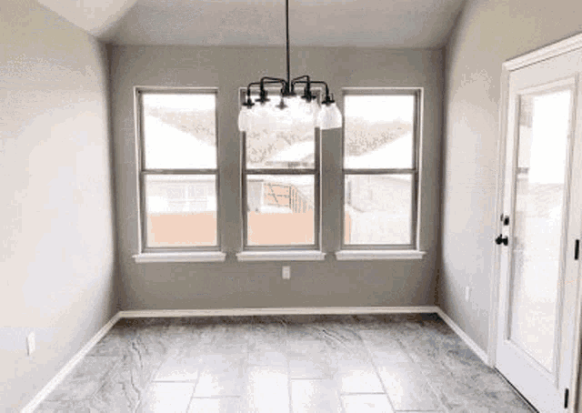 an empty dining room with a chandelier , tile floor , and three windows .
