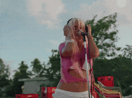 a woman singing into a microphone wearing headphones and a pink top