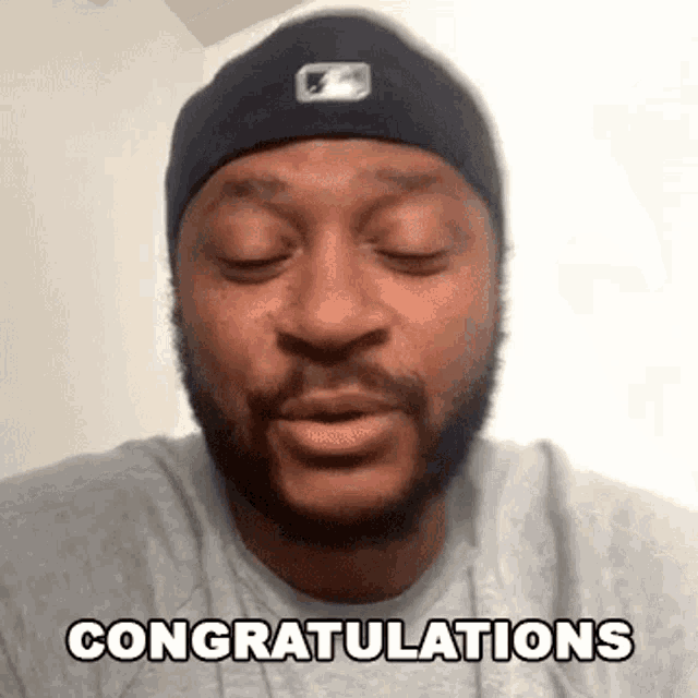 a man with a beard wearing a beanie and a gray shirt is congratulating someone with his eyes closed .