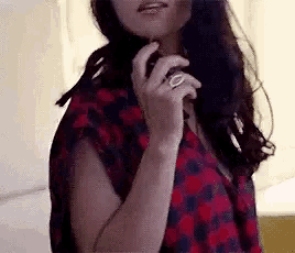 a woman wearing a plaid shirt and a ring on her finger is smoking a cigarette .