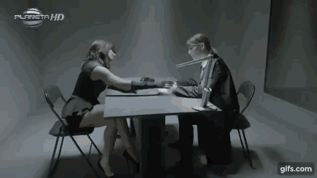 a woman sits at a table with a man in a suit and a planet hd logo behind her
