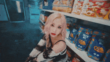 a woman is sitting in front of a shelf with snack mix on it