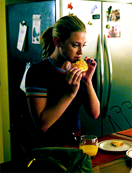 a woman is eating a sandwich in front of a refrigerator with a picture of a dog on it