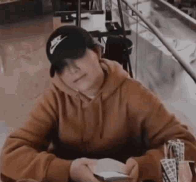 a man wearing a nike hat and a brown hoodie is sitting at a table .