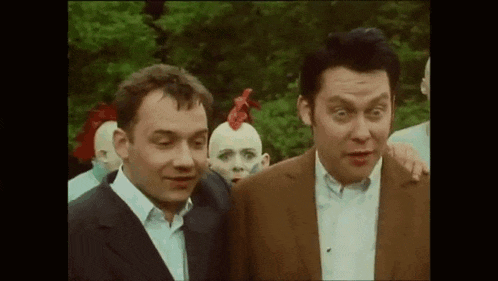 a group of men are standing next to each other in a park . one of the men has a red rooster on his head .