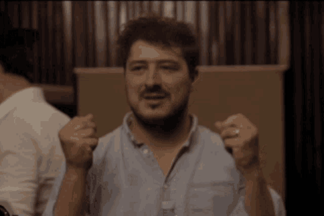 a man in a blue shirt is holding his fist up
