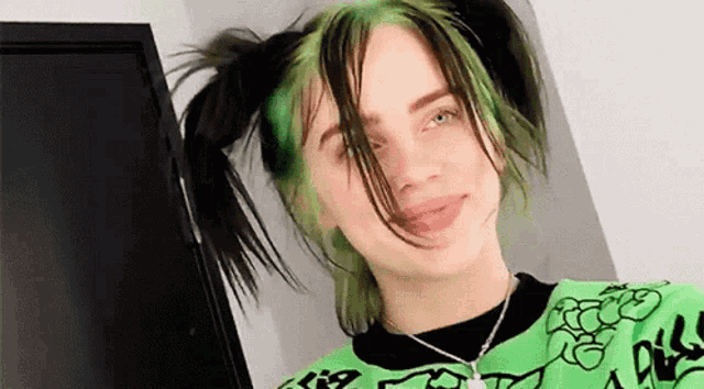 billie eilish has green hair and pigtails and is wearing a green sweater and necklace .