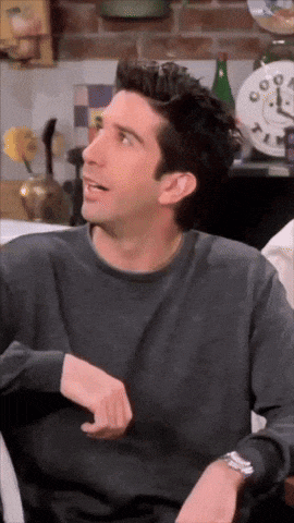 a man wearing a grey shirt and a watch is sitting in front of a clock