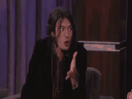 a man is sitting in a chair making a funny face while talking to another man .