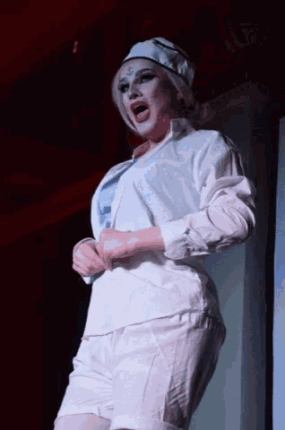 a woman in a white shirt and shorts is standing on a stage with her mouth open