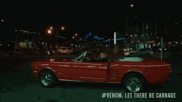 a man is driving a red car with #venom let there be carnage written on the bottom