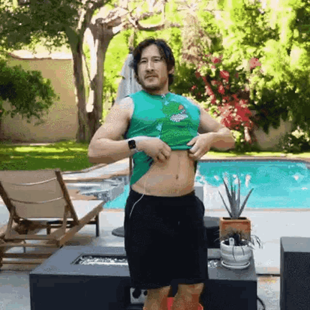 a man is standing next to a pool wearing a green tank top and black shorts .