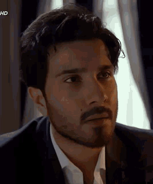 a man with a beard wearing a suit and white shirt is looking at the camera .